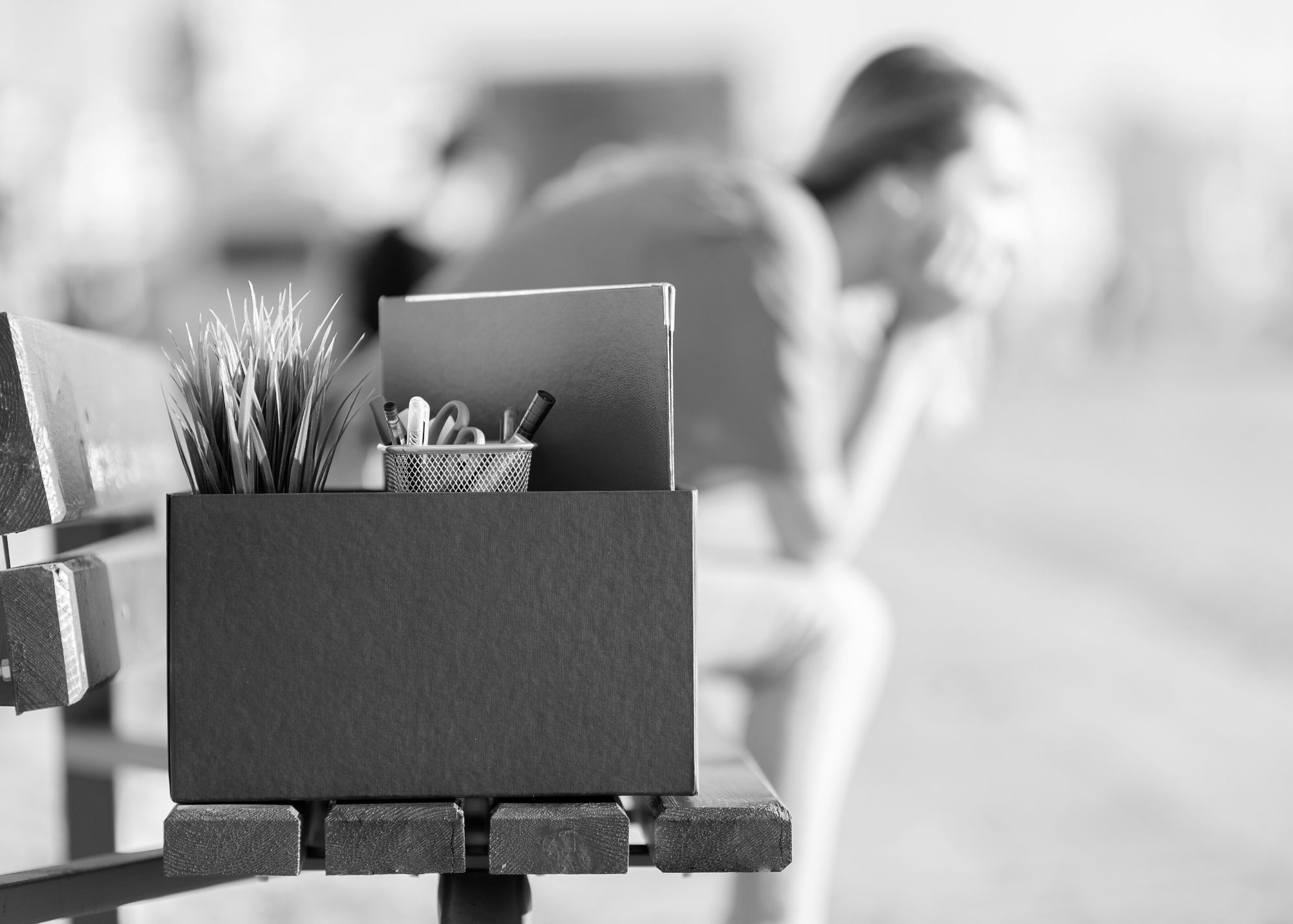 Woman on a bench with box of items from office after losing her job