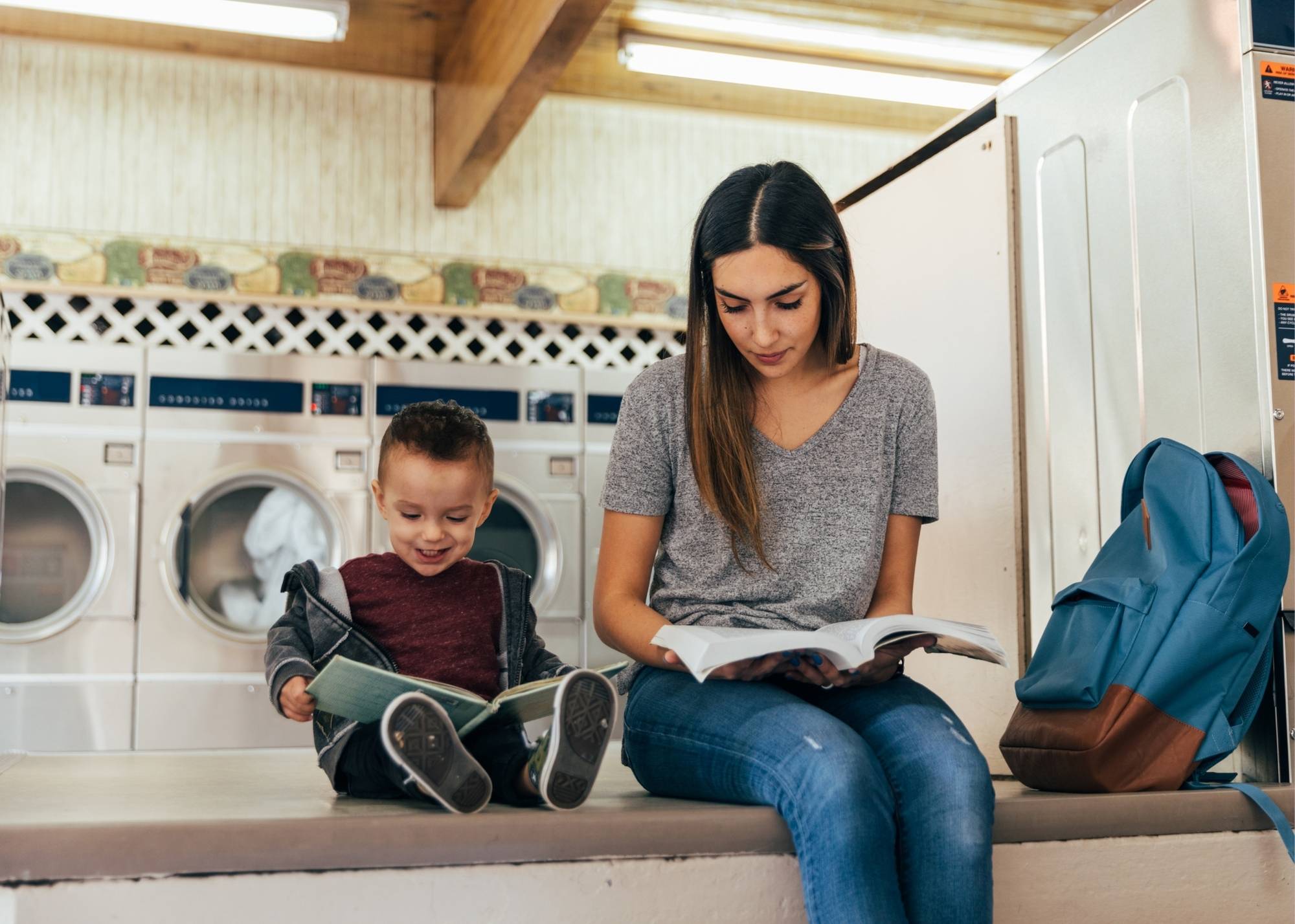 single parent woman student and son both reading at laundrymat